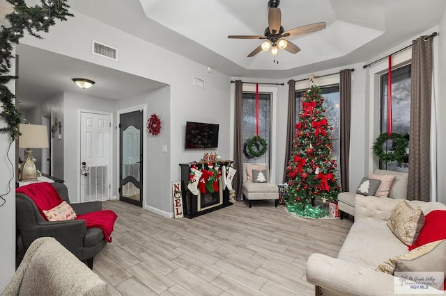 living room featuring a raised ceiling, ceiling fan, and light hardwood / wood-style floors