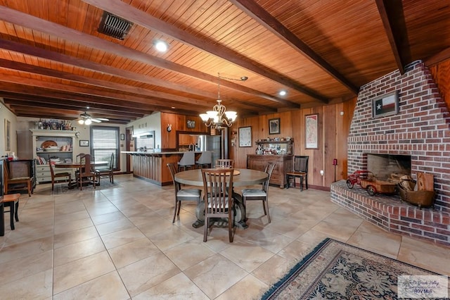 dining space with wood walls, ceiling fan with notable chandelier, beam ceiling, and wooden ceiling