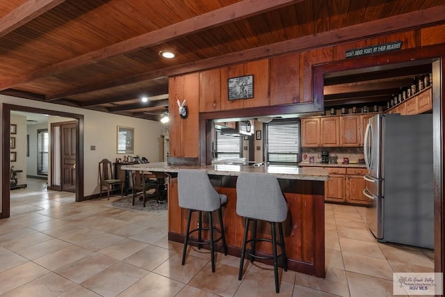 kitchen with beam ceiling, stainless steel refrigerator, light stone counters, and light tile patterned flooring