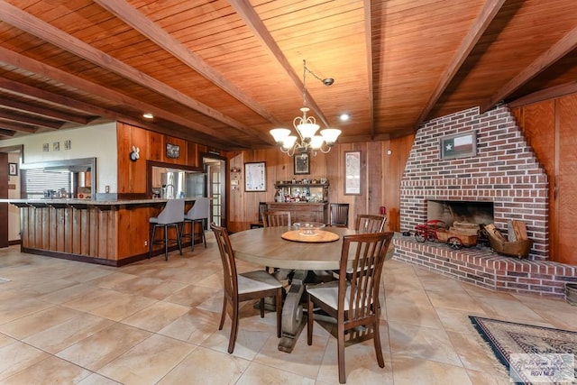 tiled dining space featuring an inviting chandelier, beamed ceiling, wooden ceiling, a fireplace, and wood walls