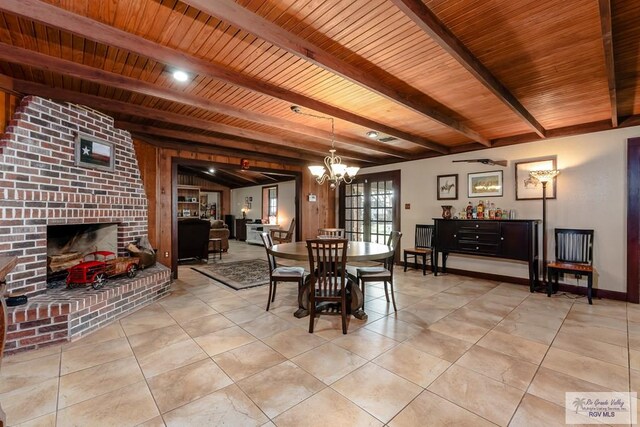 tiled dining room with a notable chandelier, beam ceiling, wooden ceiling, and a brick fireplace