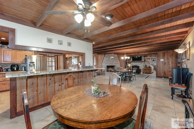 dining space featuring wood ceiling, ceiling fan with notable chandelier, beam ceiling, a fireplace, and light tile patterned flooring