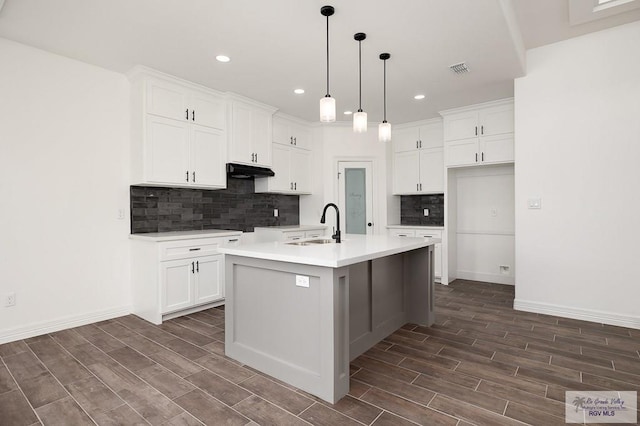 kitchen with dark wood-type flooring, sink, an island with sink, decorative light fixtures, and white cabinetry