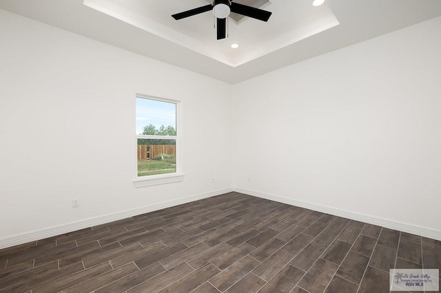 spare room with dark hardwood / wood-style floors, ceiling fan, and a raised ceiling