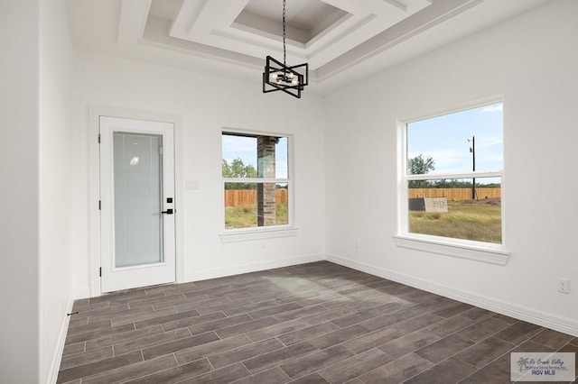 unfurnished dining area featuring dark hardwood / wood-style flooring, a raised ceiling, and a notable chandelier