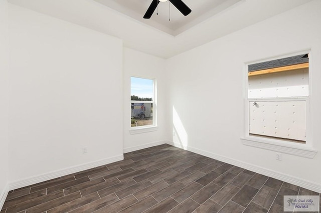 empty room with a raised ceiling, ceiling fan, and dark hardwood / wood-style flooring