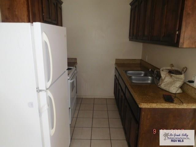 2100 Old Port Isabel Rd, Brownsville, TX 78526 - kitchen with freestanding refrigerator, a sink, light tile patterned floors, baseboards, and dark brown cabinetry