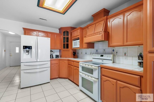 kitchen featuring decorative backsplash, premium range hood, white appliances, light tile patterned floors, and tile countertops