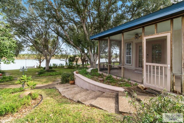 view of yard featuring a water view, ceiling fan, and a sunroom