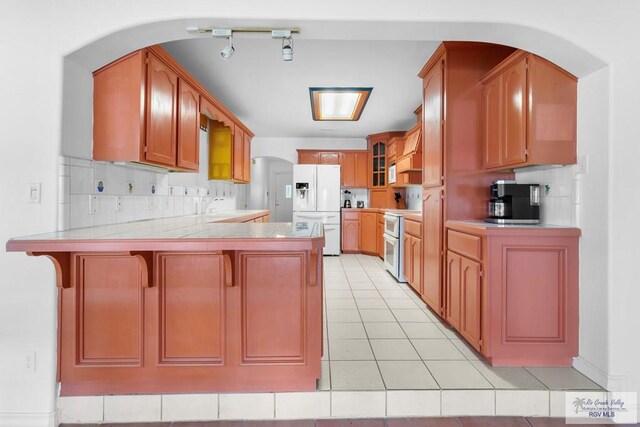 kitchen with a kitchen bar, white appliances, kitchen peninsula, and backsplash