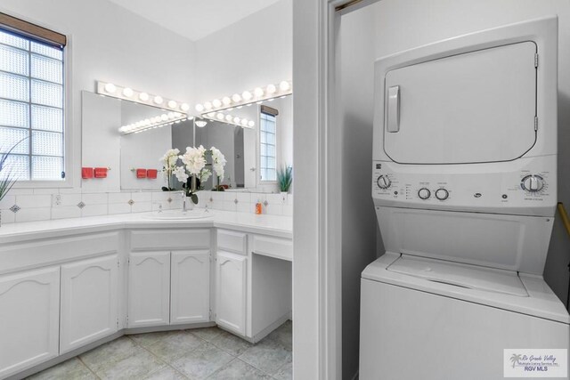 laundry room with sink, light tile patterned floors, and stacked washer and clothes dryer