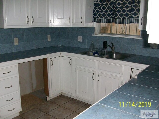 kitchen featuring tile countertops, backsplash, tile patterned floors, sink, and white cabinetry