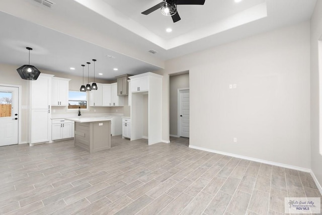 kitchen with a center island, a tray ceiling, ceiling fan, white cabinets, and pendant lighting