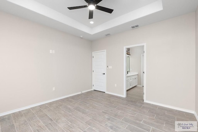 unfurnished bedroom featuring ensuite bathroom, ceiling fan, and a tray ceiling