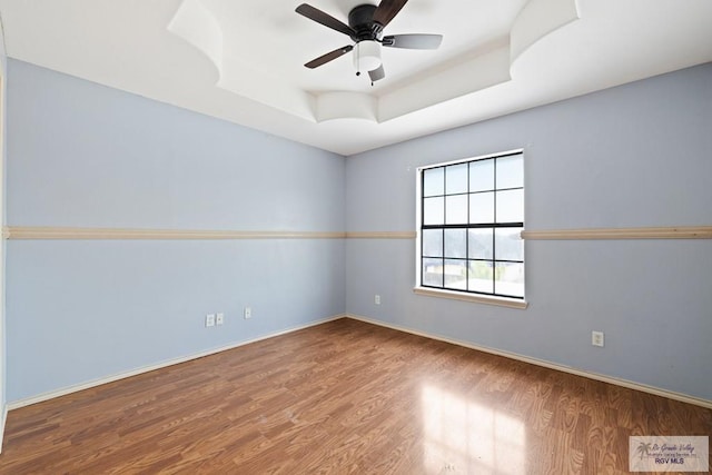 empty room with ceiling fan, wood-type flooring, and a raised ceiling