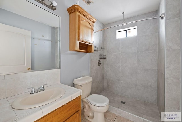 bathroom with toilet, backsplash, tile patterned floors, and a tile shower