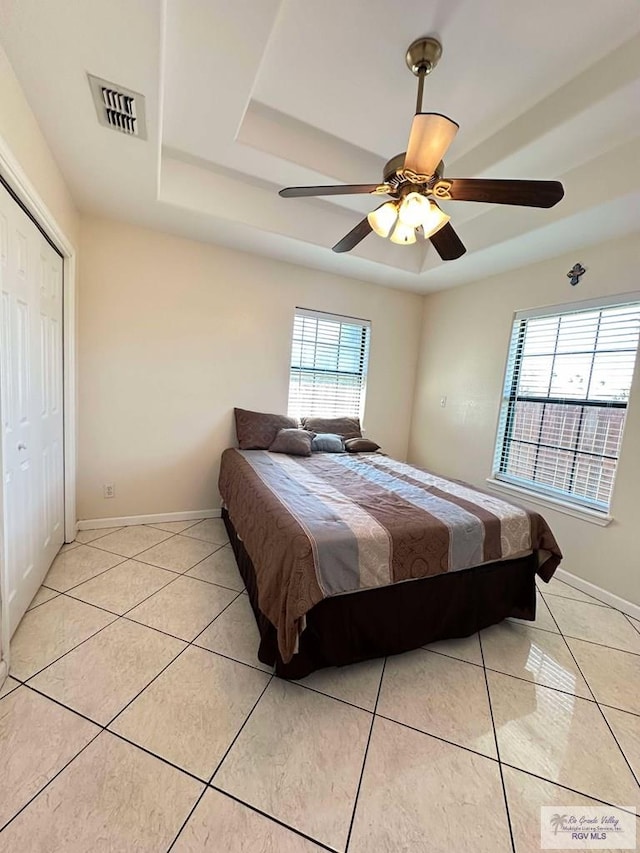 bedroom with light tile patterned floors, visible vents, a tray ceiling, and baseboards