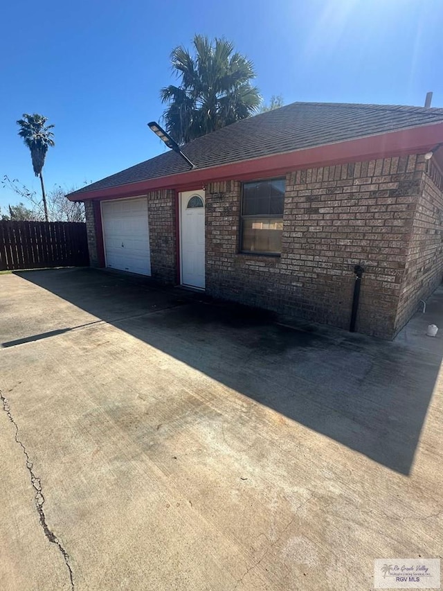 view of front of home featuring driveway, roof with shingles, an attached garage, fence, and brick siding