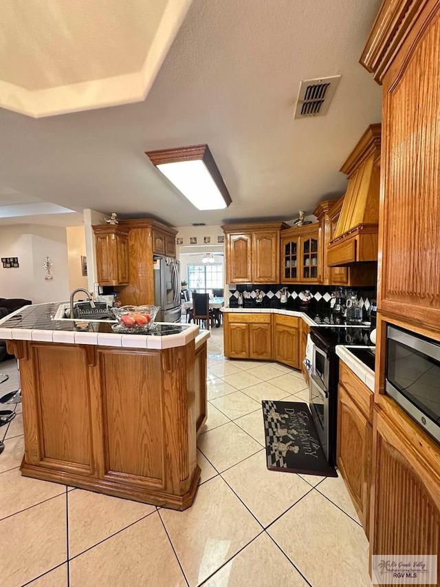 kitchen with visible vents, tile countertops, brown cabinets, custom exhaust hood, and stainless steel appliances