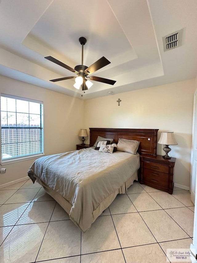 bedroom featuring light tile patterned floors, visible vents, baseboards, ceiling fan, and a tray ceiling