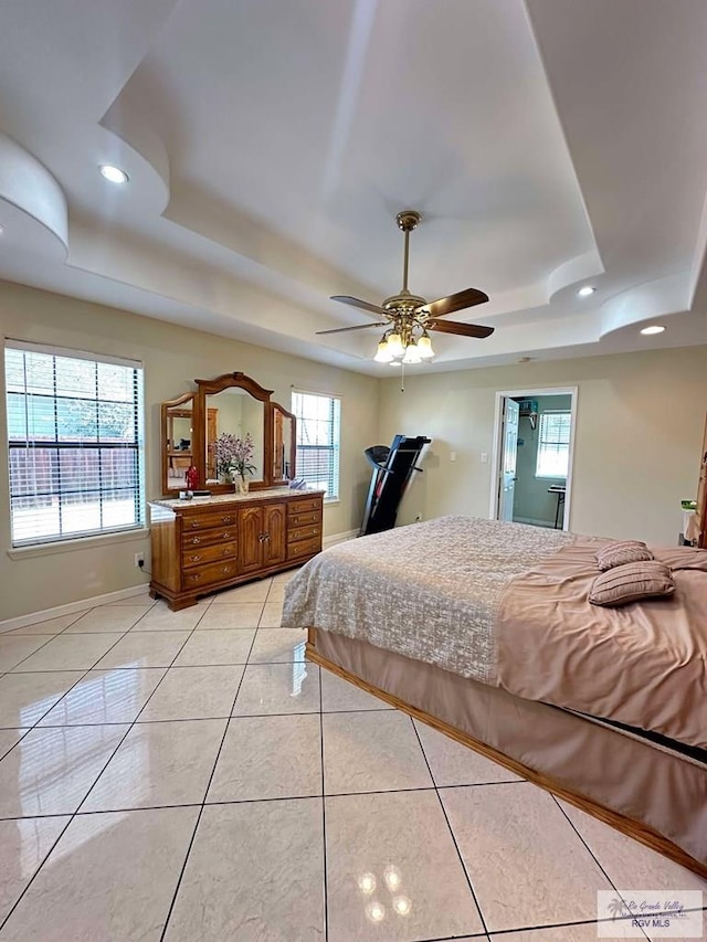 bedroom with a tray ceiling, light tile patterned flooring, and baseboards