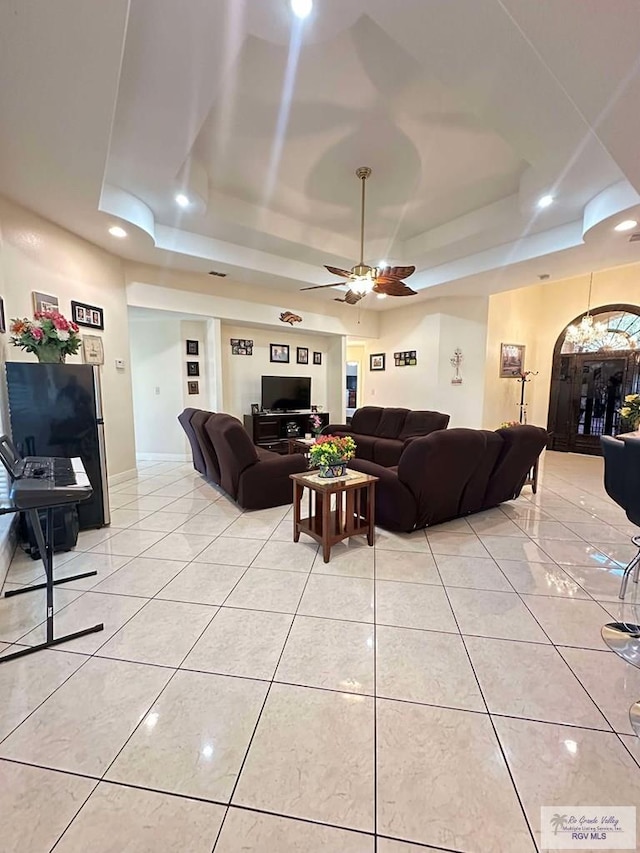 living room featuring light tile patterned floors, ceiling fan, a tray ceiling, and baseboards