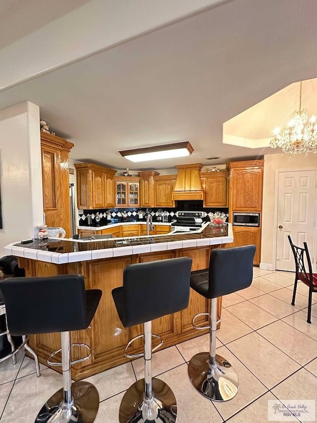 kitchen with tile counters, brown cabinets, stainless steel appliances, and a peninsula