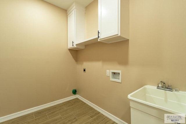laundry area featuring a sink, wood finished floors, hookup for an electric dryer, baseboards, and cabinet space