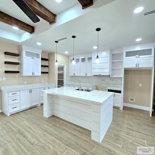 kitchen with white cabinetry, decorative light fixtures, a center island with sink, beam ceiling, and decorative backsplash