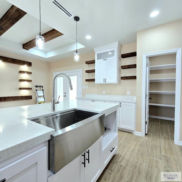 kitchen featuring light stone countertops, sink, pendant lighting, and white cabinets