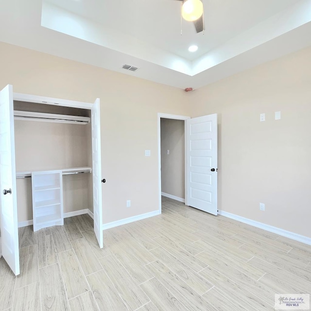 unfurnished bedroom featuring a closet, light hardwood / wood-style floors, a raised ceiling, and ceiling fan