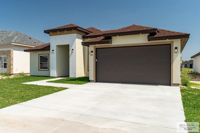 prairie-style home with a front yard, roof with shingles, concrete driveway, stucco siding, and a garage