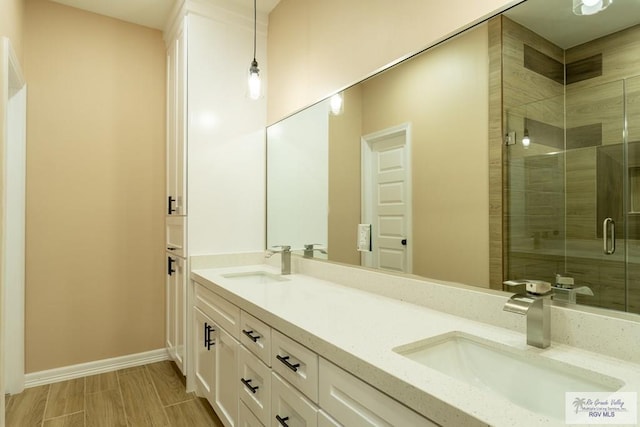 full bath featuring a stall shower, double vanity, baseboards, and a sink