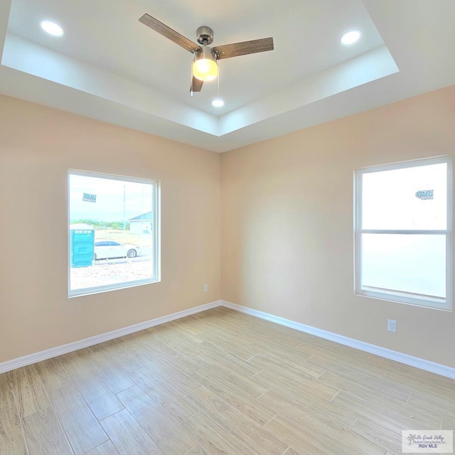 spare room with ceiling fan, a raised ceiling, and light wood-type flooring