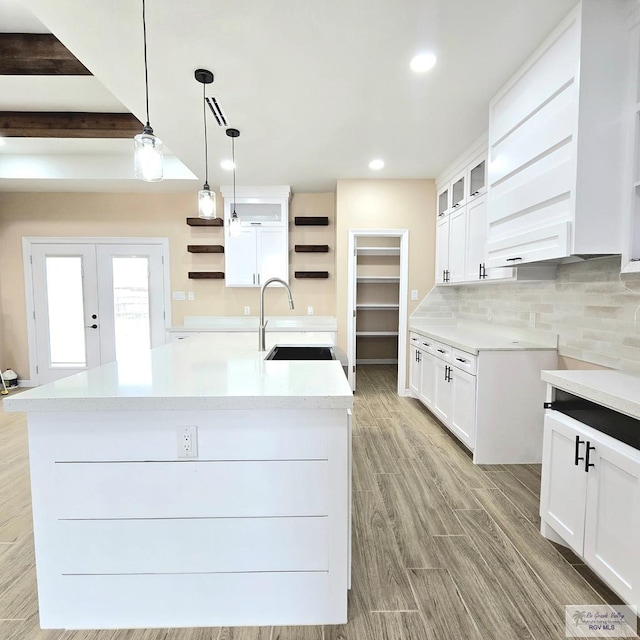 kitchen with sink, white cabinetry, decorative backsplash, a center island with sink, and decorative light fixtures