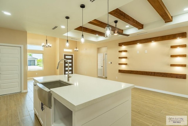 kitchen with light countertops, light wood-style flooring, beam ceiling, and a sink