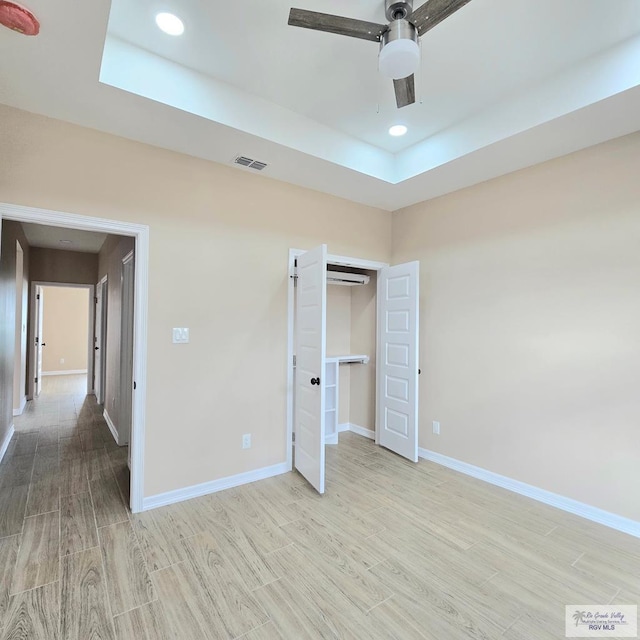 unfurnished bedroom featuring ceiling fan, a raised ceiling, and light hardwood / wood-style flooring