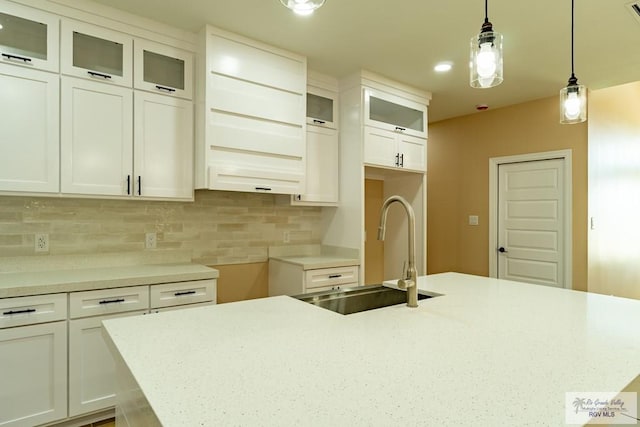 kitchen featuring white cabinets, a center island with sink, a sink, decorative light fixtures, and backsplash