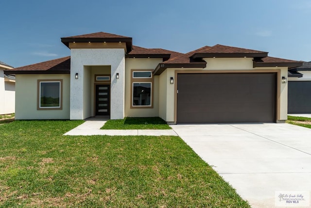 prairie-style home with driveway, a front yard, roof with shingles, stucco siding, and an attached garage