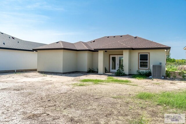rear view of house with stucco siding, a shingled roof, central AC unit, and french doors