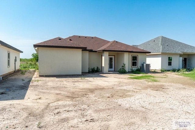 rear view of house featuring central AC unit, a shingled roof, and stucco siding