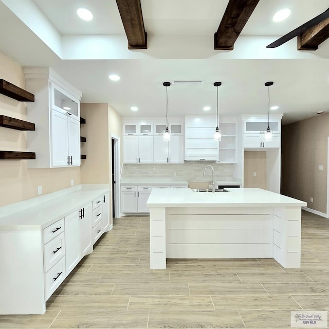 kitchen with sink, an island with sink, white cabinets, decorative backsplash, and decorative light fixtures