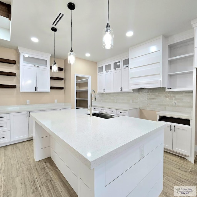 kitchen with backsplash, white cabinets, sink, and a large island with sink