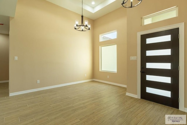 entrance foyer with a chandelier, light wood finished floors, baseboards, a towering ceiling, and recessed lighting