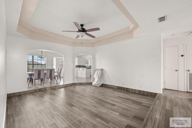 3673 Rey Enrique Dr, Brownsville, TX 78521 - empty room featuring arched walkways, a raised ceiling, a ceiling fan, wood finished floors, and a chandelier
