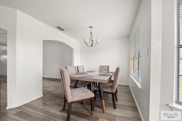 3673 Rey Enrique Dr, Brownsville, TX 78521 - dining room featuring a chandelier, arched walkways, baseboards, wood finished floors, and healthy amount of natural light