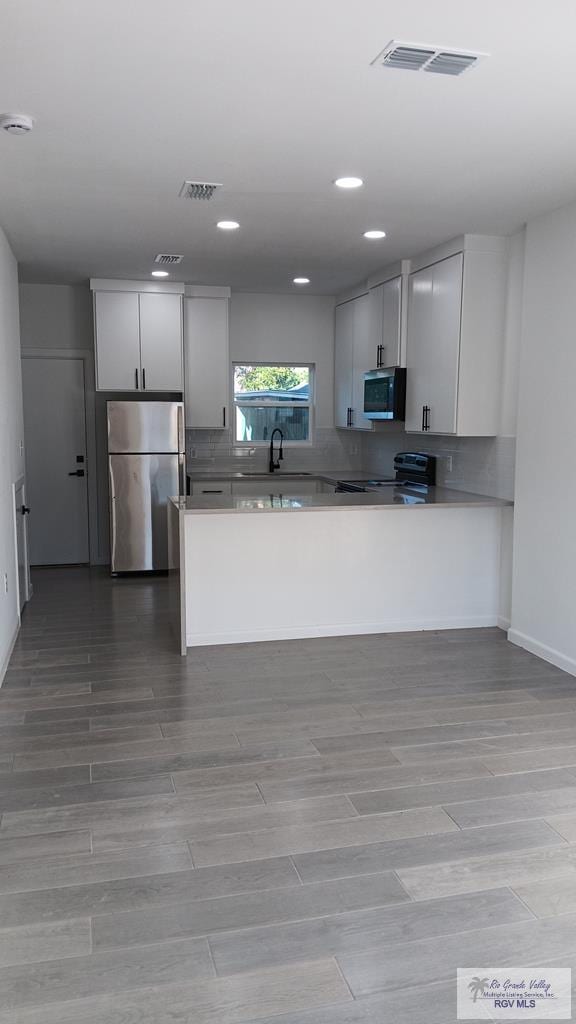 kitchen featuring kitchen peninsula, stainless steel appliances, white cabinets, and sink