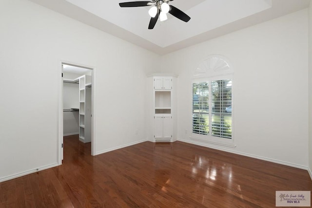 unfurnished bedroom with a walk in closet, ceiling fan, a closet, and dark wood-type flooring