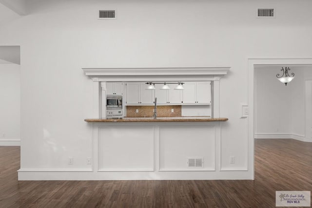 interior space with stainless steel microwave, tasteful backsplash, dark hardwood / wood-style flooring, pendant lighting, and white cabinets