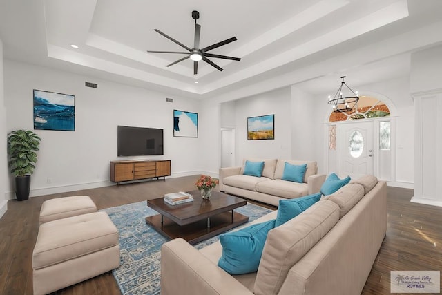 living room with a tray ceiling, ceiling fan with notable chandelier, and dark hardwood / wood-style floors